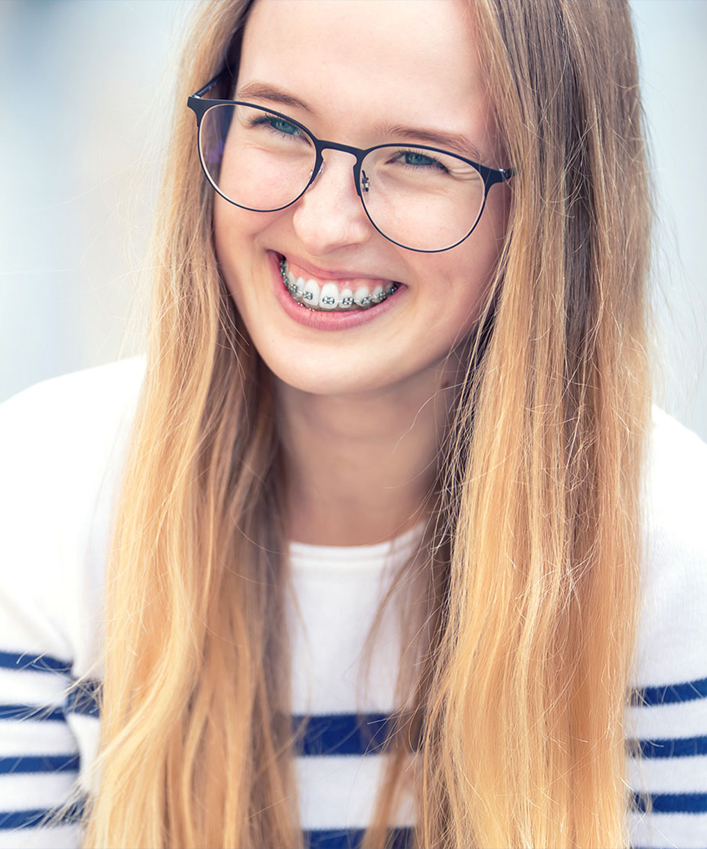 Een vrolijke vrouw met bril en beugel lacht.