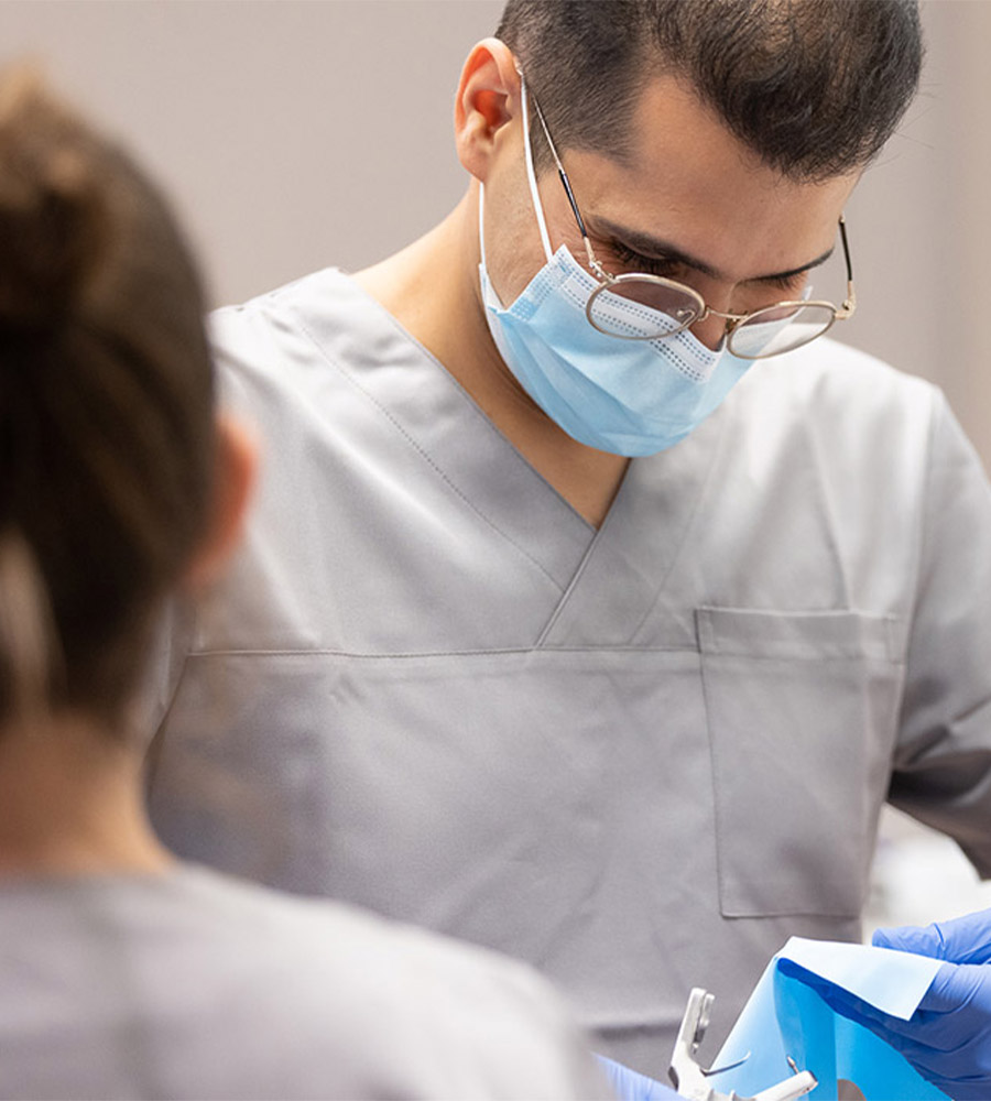 Een tandarts met een chirurgisch masker en bril werkt aan een pati&euml;nt.
